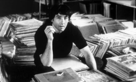 Film still from "High Fidelity", a man sitting next to various stacks of books