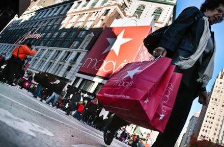 Older woman holding a Macy's red bag while crossing the street before Thanksgiving