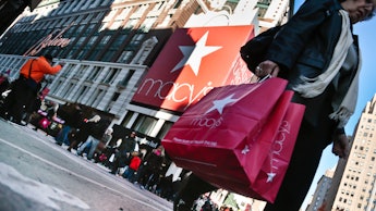 Older woman holding a Macy's red bag while crossing the street before Thanksgiving