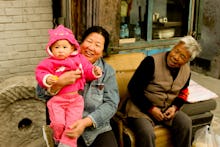 Asian parents sitting outside while holding their daughter who is in a pink puff jacket