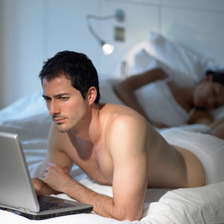A man exploring a site on his laptop while in bed with his partner