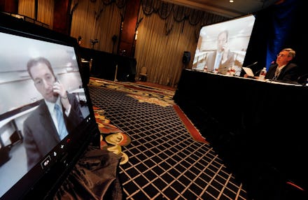 A man sitting next to a desk and a screen with another man on a live video call during a journalism ...