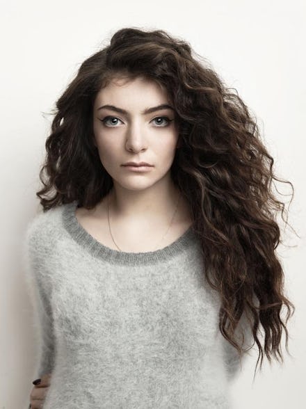 Lorde in a grey sweater standing in front of a white wall