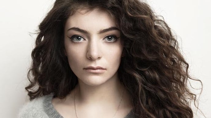Lorde in a grey sweater standing in front of a white wall