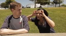 An Asian woman mocking a white man by spreading her eyelids to look wider to show what it is like wh...