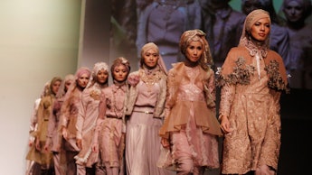 Models walking on the runway wearing hijabs and modest clothing in beige and grey tones