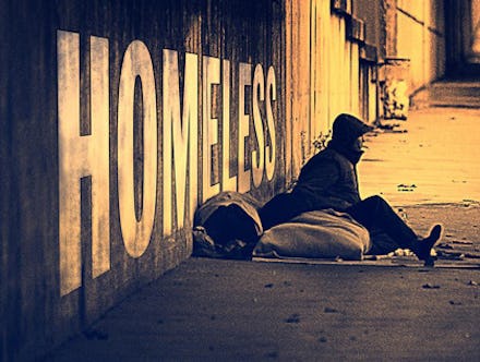 A homeless person with their sleeping bag sitting in front of the sign on the wall that says "HOMELE...