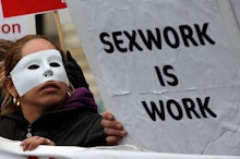 A woman with a white mask in a protest and a poster with the text 'Sexwork is work'