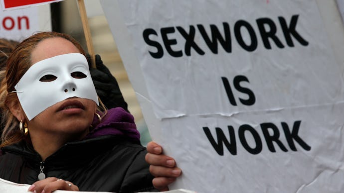 A woman with a white mask in a protest and a poster with the text 'Sexwork is work'