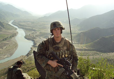 A marine corps soldier standing in front of a mountain range holding his rifle