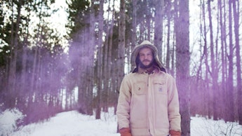 Justin Vernon from Bon Iver band in a white jacket in the middle of a forest full of snow
