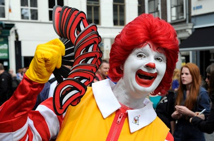 A fast food worker dressed as Ronald McDonald holding cutouts of his smile to hand out