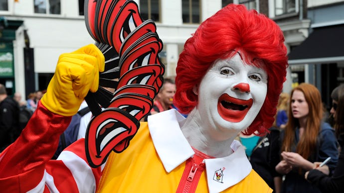 A fast food worker dressed as Ronald McDonald holding cutouts of his smile to hand out