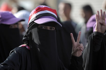 Younger woman wearing black mask and cap holding peace sign