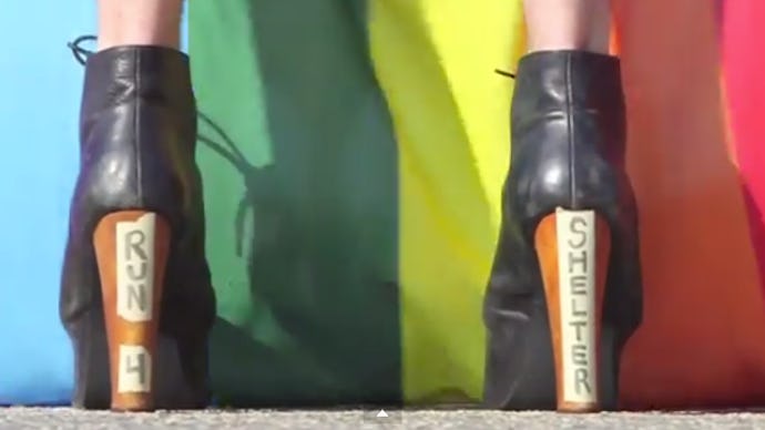 A person in heels with the text 'RUN 4 SHELTER' in front of a LGBTQ Youth flag