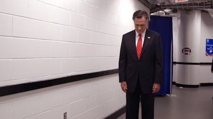 Mitt Romney standing in a black suite and red tie looking at the floor