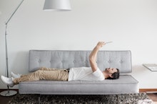 man in white sneakers, beige pants and a white shirt lying on his couch and looking at his phone