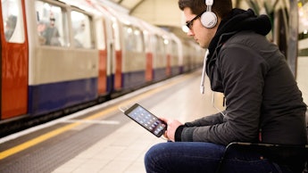 A man listening to music from his phone through his headphones while at a subway station