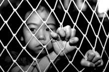 A child victim of human trafficking holding onto a fence