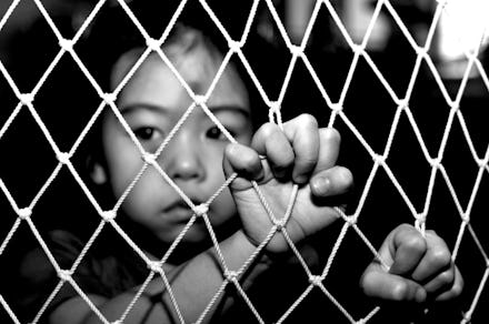 A child victim of human trafficking holding onto a fence