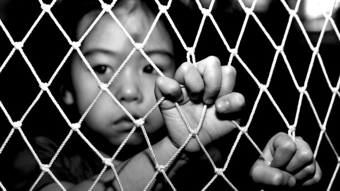 A child victim of human trafficking holding onto a fence