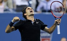 Roger Federer in a black shirt, and holding a racket looking up