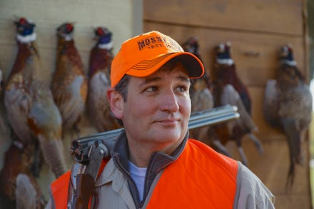 Ted Cruz with a hunting riffle on his shoulder and ducks hanging on a wall behind him