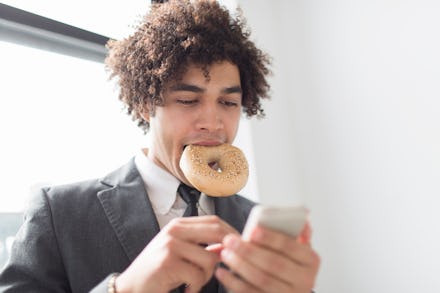 A man typing on his phone while having a breakfast bagel in his mouth