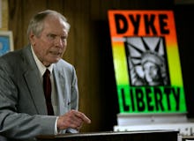 Fred Phelps in a grey suit and a poster with the text 'Dyke Liberty' in the background