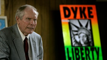 Fred Phelps in a grey suit and a poster with the text 'Dyke Liberty' in the background