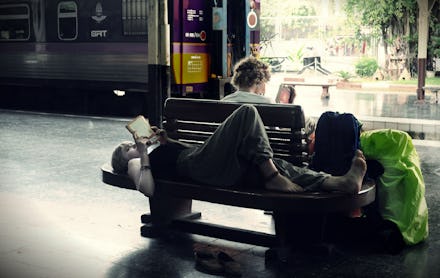Two 20-something-year-olds reading books on a bench, one is laying down and the other is sitting  