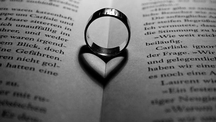 A ring put between two pages of a book with its shadow forming a heart shape