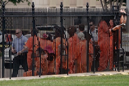 Prisoners behind the fence at the yard of Guantánamo Bay with a police officer