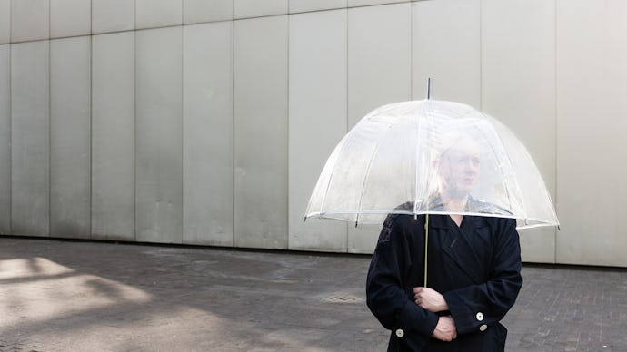 A trans person standing in a black coat and holding a see-through umbrella