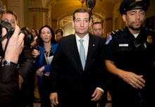 Ted Cruz walking down a hall with reporters taking pictures and asking him questions as he's escorte...