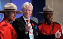 Bill de Blasio giving a thumbs up and pointing while standing next to two canadian mounties