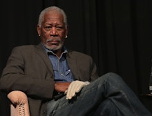Morgan Freeman sitting in a chair with his legs crossed and a white glove on his left hand