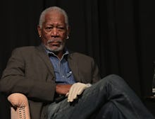 Morgan Freeman sitting in a chair with his legs crossed and a white glove on his left hand