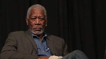 Morgan Freeman sitting in a chair with his legs crossed and a white glove on his left hand