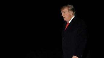 Donald Trump walking, looking angry with a black background behind him, in a black suit with a white...