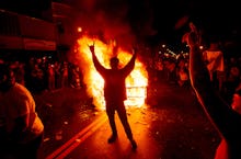 A group of fans rioting after a championship team while a fire rages on the street