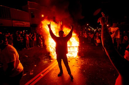 A group of fans rioting after a championship team while a fire rages on the street