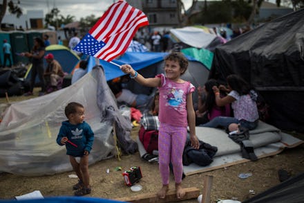 A girl waving an american flag in an immigration camp while other children run around 