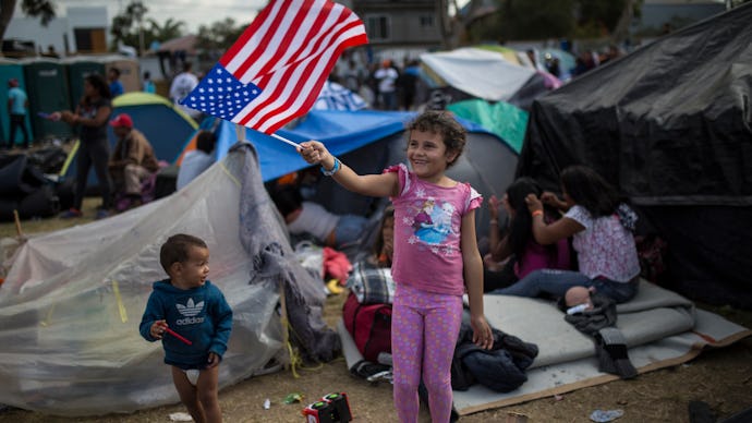 A girl waving an american flag in an immigration camp while other children run around 