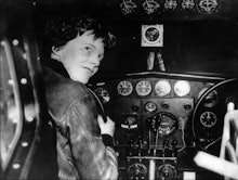 An old black and white image of Amelia Earhart sitting at the cockpit of a plane
