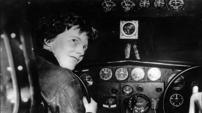 An old black and white image of Amelia Earhart sitting at the cockpit of a plane