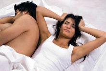 Woman holding her head in stress while laying in bed with a man