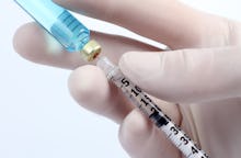 Closeup of a hand wearing a surgical glove and extracting a vaccine from the bottle with a syringe