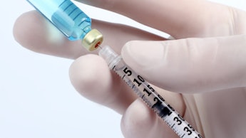 Closeup of a hand wearing a surgical glove and extracting a vaccine from the bottle with a syringe