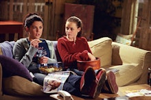 Lorelai and Rory from 'Gilmore Girls' sitting on a couch and eating popcorn as Rory's mom is her bes...